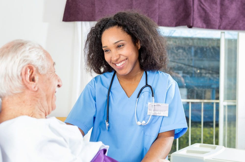 A nurse smiling at an older man in blue scrubs.