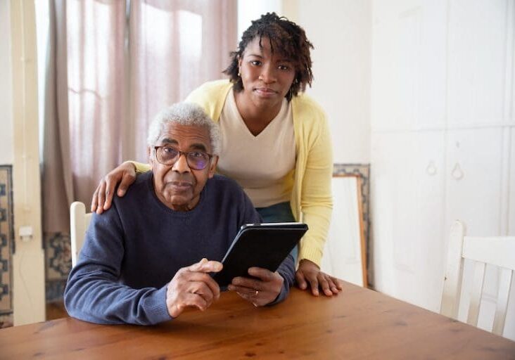 A woman standing next to an older man holding a tablet.